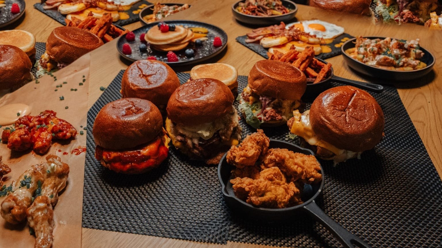 A table covered in N.A.D.H burgers, fried chicken, wings and pancakes